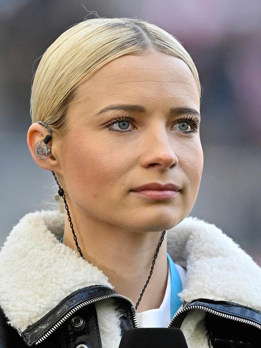 Moderatorin Lena Cassel mit In-Ear.Kopfhörern auf dem Fußballplatz