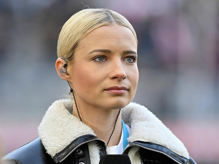 Moderatorin Lena Cassel mit In-Ear.Kopfhörern auf dem Fußballplatz