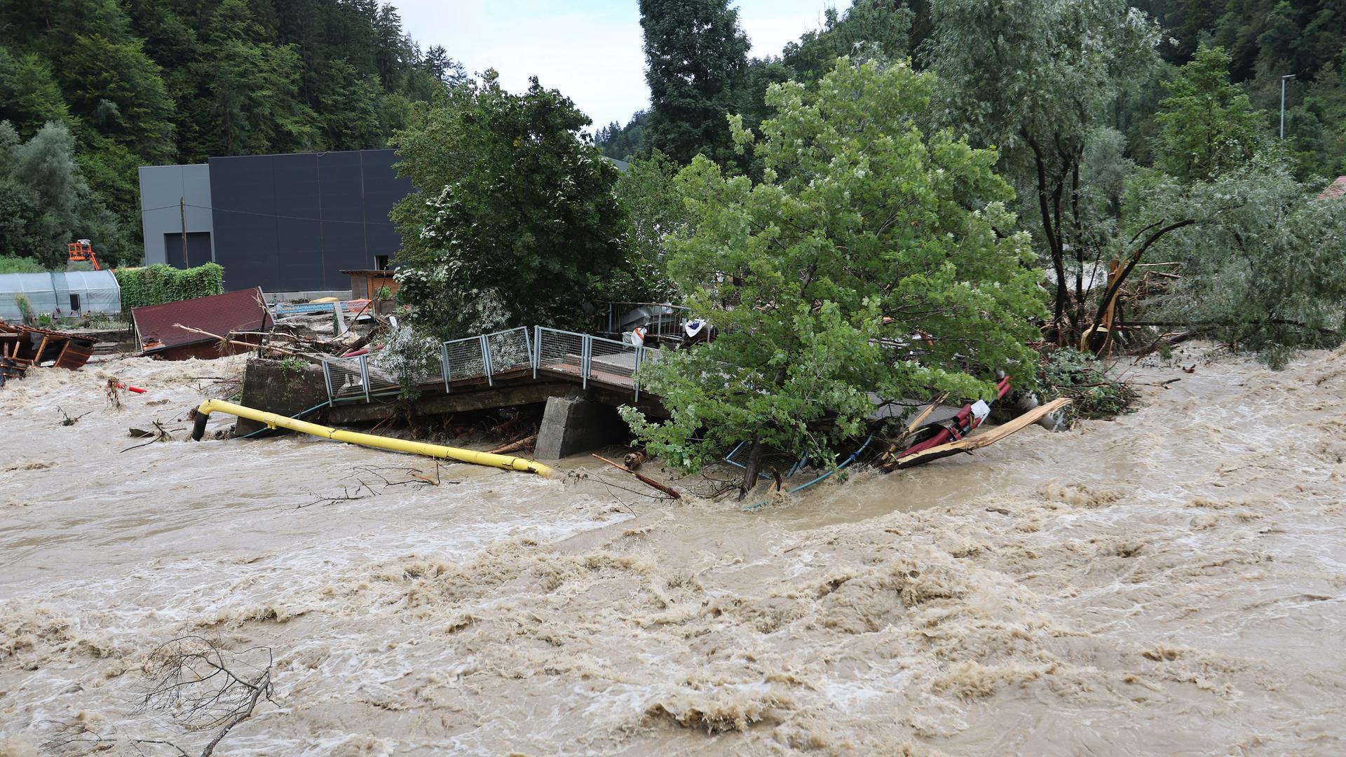 Überflutung in Prevalje in Slowenien am 6.August 2023. Das Bild zeigt Häuser und eine Brücke, die vom Wasser zerstört werden.