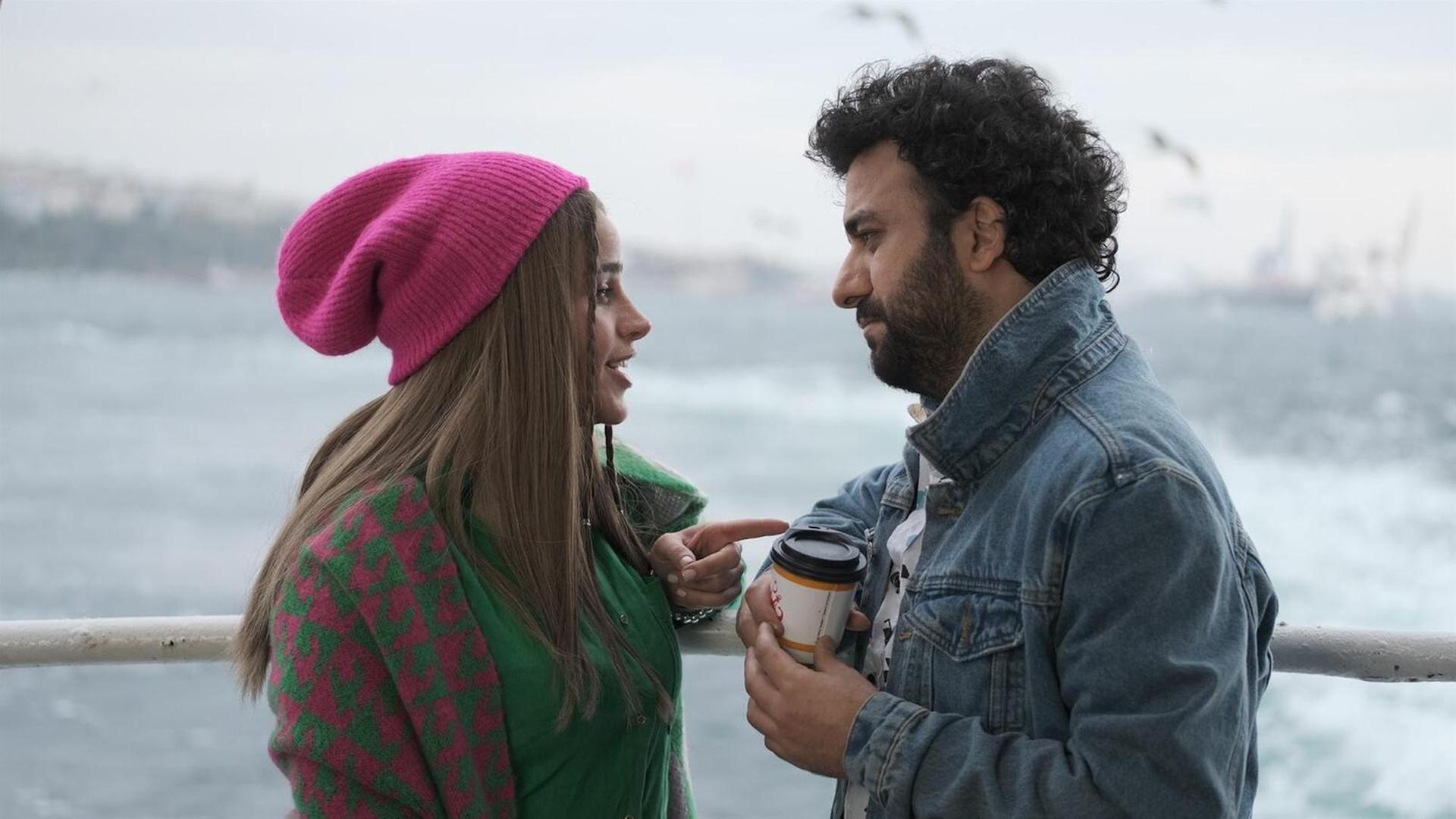 Im Still aus "Çok Aşk" stehen sich eine Frau mit pinker Mütze und ein lockiger Mann mit Kaffeebecher in der Hand gegenüber, während sie spricht und er sie betreten anschaut.