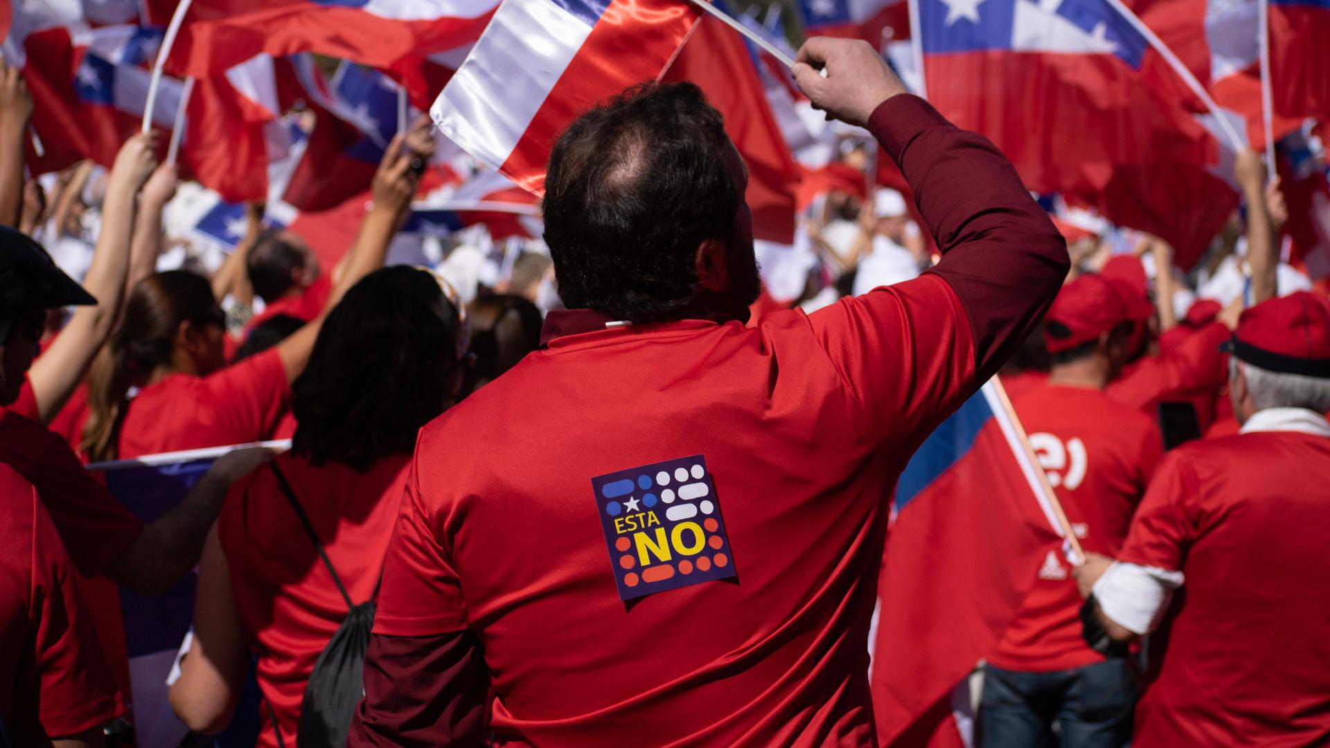 Viele Menschen mit chilenischen Fahnen und roten T-Shirts auf denen hinten "Nein" steht versammeln sich in großen Ansammlungen.