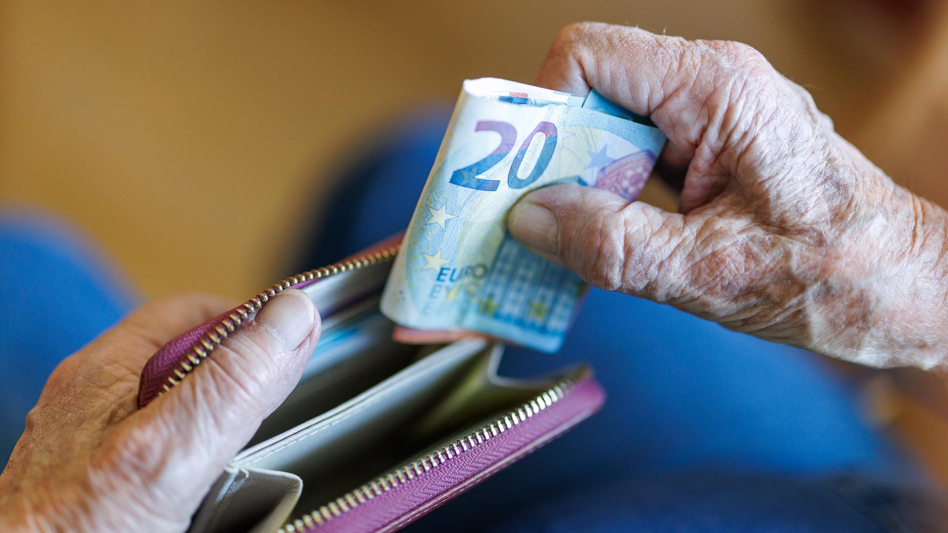 Die Hände eines älteren Menschen stecken Geldscheinen in ein Portemonnaie.