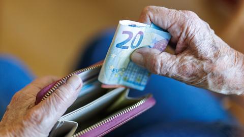 Die Hände eines älteren Menschen stecken Geldscheinen in ein Portemonnaie.