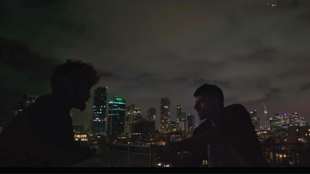 Zwei Männer sind im Profil zu erkennen. Sie sitzen im Dunkeln draußen. Im Hintergrund ist die Skyline von Tel Aviv zu erkennen. Es handelt sich um eine Szene aus der Doku "NAZA". Zwei Männer sind im Profil zu erkennen. Sie sitzen im Dunkeln draußen. Im Hintergrund ist die Skyline von Tel Aviv zu erkennen. Es handelt sich um eine Szene aus der Doku "NAZA".