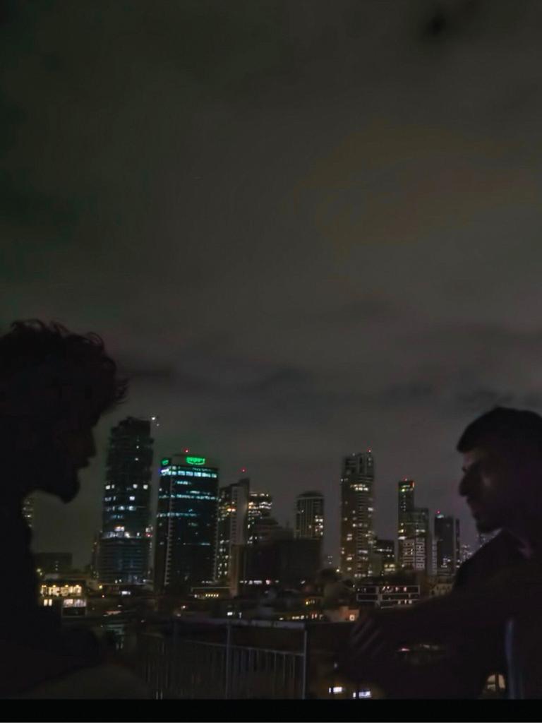 Zwei Männer sind im Profil zu erkennen. Sie sitzen im Dunkeln draußen. Im Hintergrund ist die Skyline von Tel Aviv zu erkennen. Es handelt sich um eine Szene aus der Doku "NAZA".