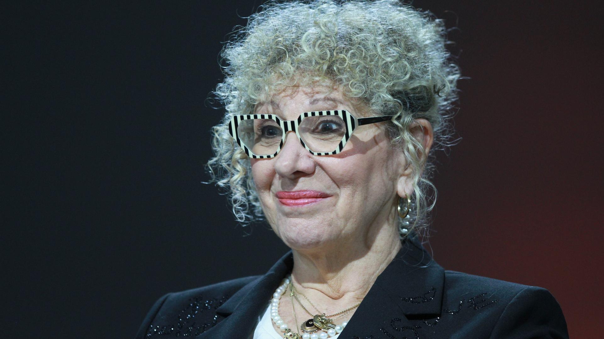 Ein Foto der Schriftstellerin Lizzie Doron aufgenommen am 21.10.2023 auf der Frankfurter Buchmesse. Sie sitzt vor einem schwarzen Hintergrund, wahrscheinlich einer Bühne, hat ein leichtes Lächeln auf den Lippen und trägt eine auffällige Brille. Ein Foto der Schriftstellerin Lizzie Doron aufgenommen am 21.10.2023 auf der Frankfurter Buchmesse. Sie sitzt vor einem schwarzen Hintergrund, wahrscheinlich einer Bühne, hat ein leichtes Lächeln auf den Lippen und trägt eine auffällige Brille.