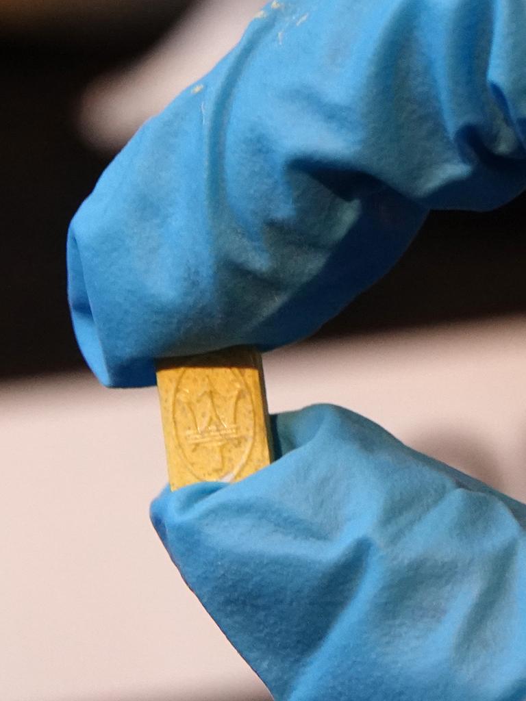 Gelbe Ecstasy-Tablette wird mit zwei Fingern in blauen Handschuhen gehalten