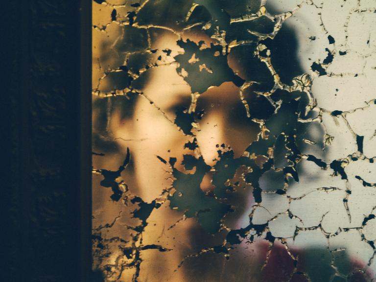 Eine junge Frau schaut in einen kaputten Spiegel.