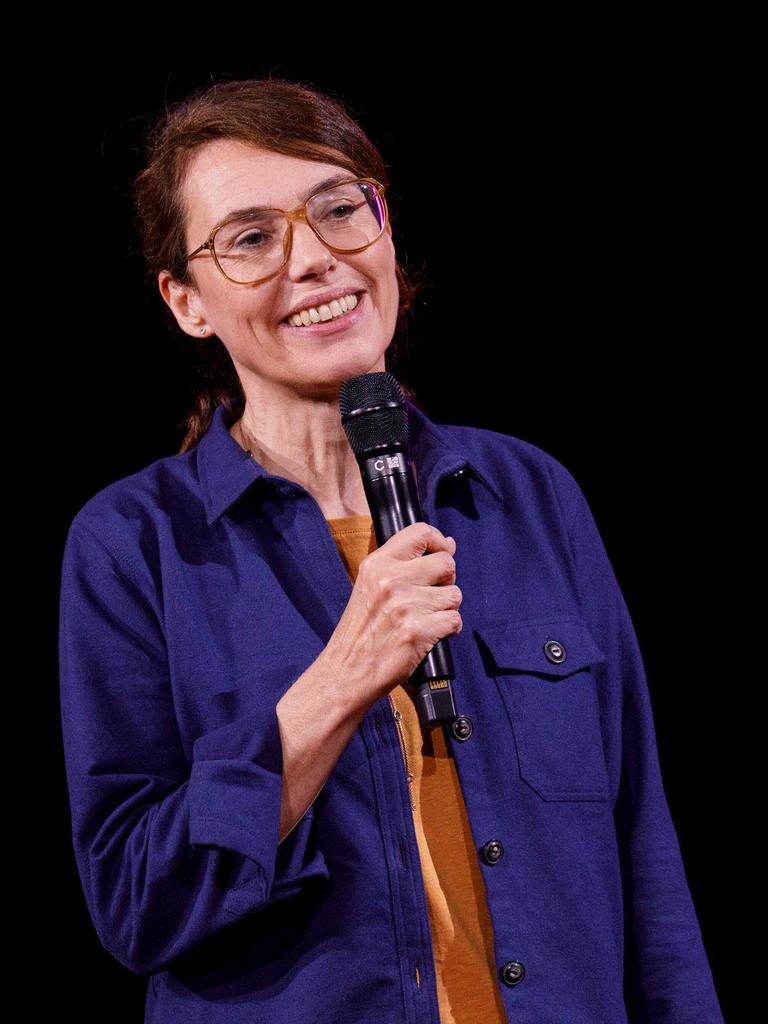 Regina Schilling steht mit einem Mikrofon in der Hand auf einer Bühne. Sie trägt dunkles langes Haar in einem Zopf gebunden und ein dunkelblaues Hemd.
