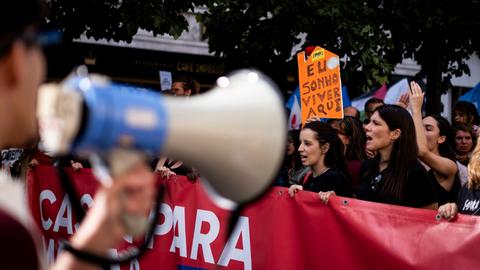 Zahlreiche Menschen laufen bei einer Demonstration mit Transparenten durch die Straßen; im Vordergrund ein unscharfes Megafon.