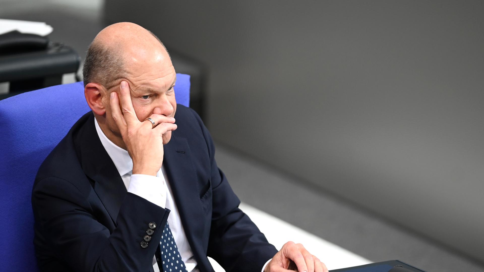 Bundeskanzler Olaf Scholz sitzt auf der Regierungsbank im Bundestag. Er stützt seinen Kopf mit der Hand ab und macht einen nachdenklichen Eindruck.