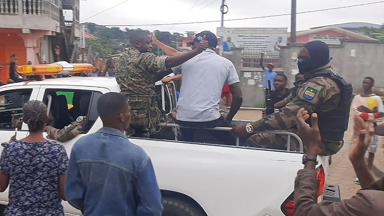 Gabun, Libreville: Soldaten sitzen auf einem offenen Pickup und Menschen um sie herum jubeln.