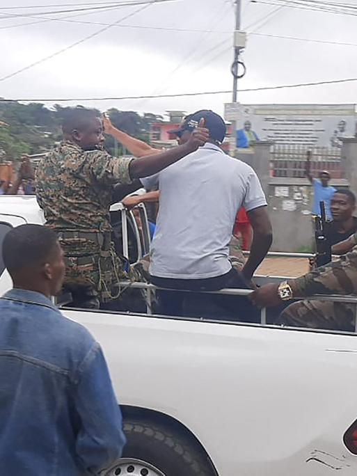 Gabun, Libreville: Soldaten sitzen auf einem offenen Pickup und Menschen um sie herum jubeln. 