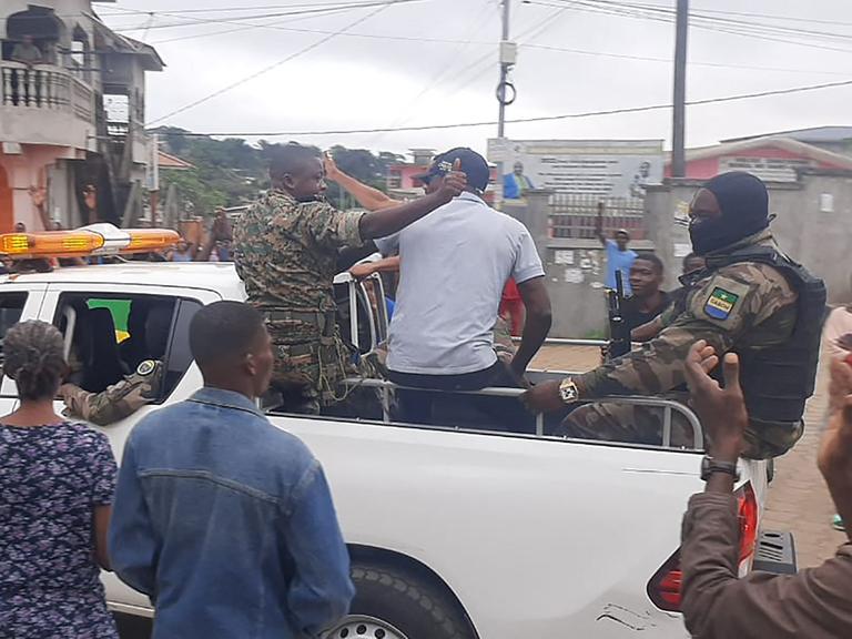 Gabun, Libreville: Soldaten sitzen auf einem offenen Pickup und Menschen um sie herum jubeln. 