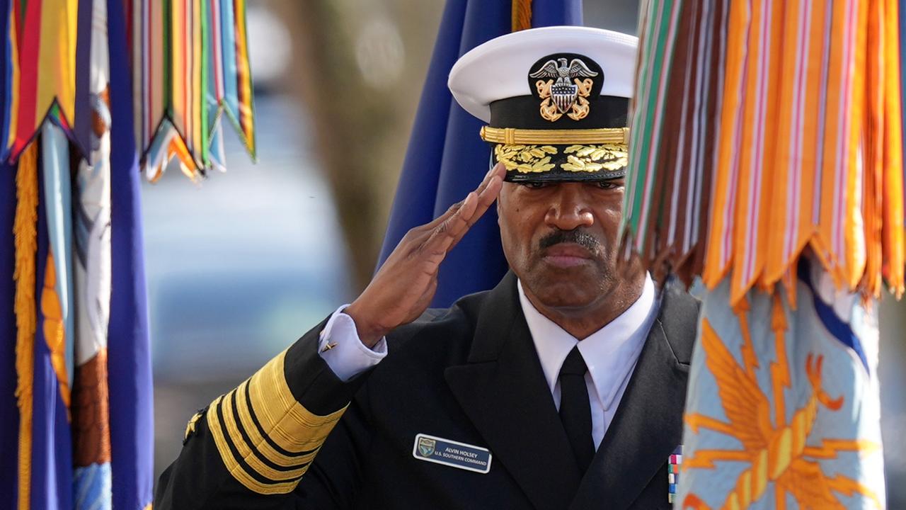 Das Bild zeigt Holseys Oberkörper in Paradeuniform. Er salutiert mit ernstem Blick. Neben ihm Fahnen von Armeeinheiten. Das Bild zeigt Holseys Oberkörper in Paradeuniform. Er salutiert mit ernstem Blick. Neben ihm Fahnen von Armeeinheiten.