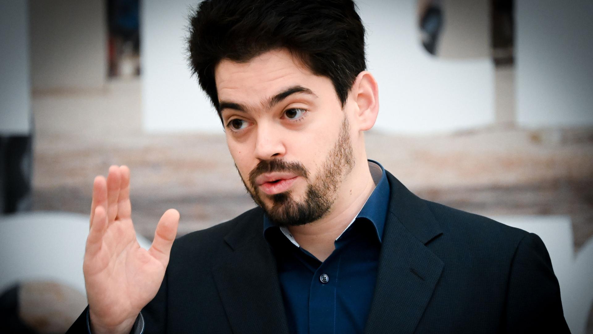 Der Dirigent Lahav Shani erhebt mit ernster Miene seine Hand. Der Dirigent Lahav Shani erhebt mit ernster Miene seine Hand.