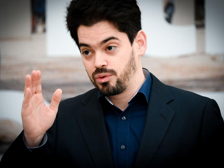 Der Dirigent Lahav Shani erhebt mit ernster Miene seine Hand.