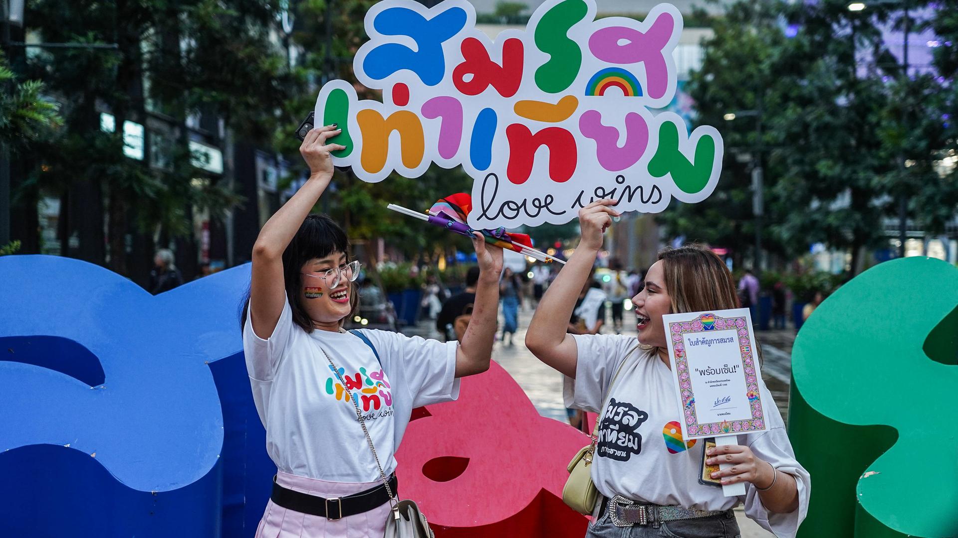 Zwei Frauen halten bunte Schilder mit der Aufschrift Love Wins (Liebe gewinnt) in die Luft.