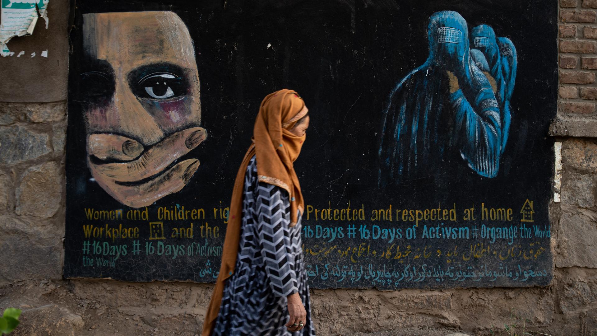 Eine verschleierte Frau geht an einem Wandgemälde vorbei, das Rechte von Frauen und Kindern in Afghanistan einfordert.