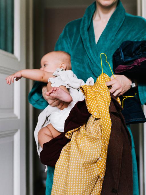 Eine Mutter hält ihr Baby und ihre Anziehsachen in den Armen.