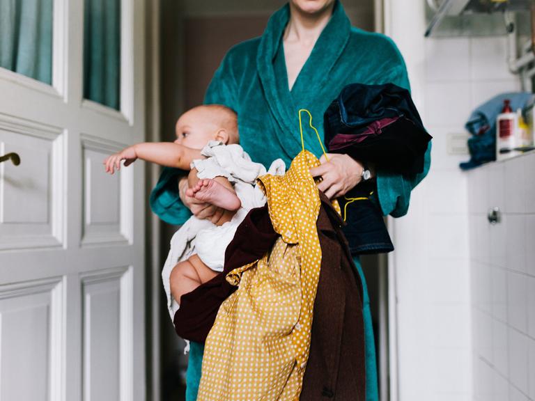Eine Mutter hält ihr Baby und ihre Anziehsachen in den Armen.
