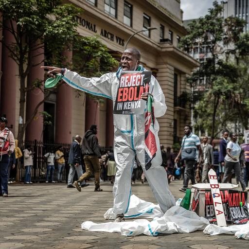 Ein Protestzug auf einer Straße, ein Mann im Vordergrund hält ein Schild mit der Aufschrift "Reject Ebola in Kenia" nach vorne.