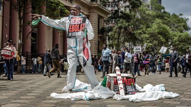 Ein Protestzug auf einer Straße, ein Mann im Vordergrund hält ein Schild mit der Aufschrift "Reject Ebola in Kenia" nach vorne.