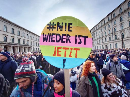Eine Menschenmenge in einer Münchener Straße, im Vordergrund ein buntes rundes Plakat mit der Aufschrift "#Nie wieder ist jetzt" Eine Menschenmenge in einer Münchener Straße, im Vordergrund ein buntes rundes Plakat mit der Aufschrift "#Nie wieder ist jetzt"