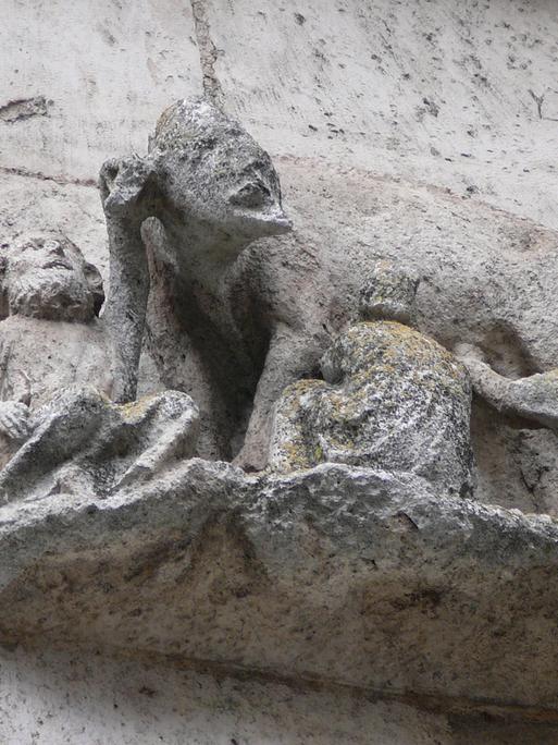 Steinernes Relief einer Sau mit menschlichem Gesicht, an deren Zitzen Männer trinken.