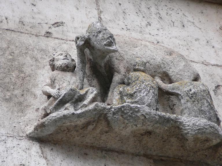 Steinernes Relief einer Sau mit menschlichem Gesicht, an deren Zitzen Männer trinken.
