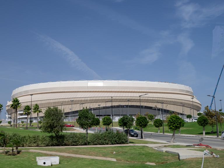 Das Fußballstadion von Tanger, welches bereits für die Weltmeisterschaft 2030 renoviert wird, ist ein helles Stadiongebäude umgeben von Rasen und Bäumen.