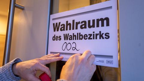 Ein Wahlhelfer hängt einen Wegweiser zum Wahlraum für die vorgezogene Wahl zum 21. Deutschen Bundestag auf