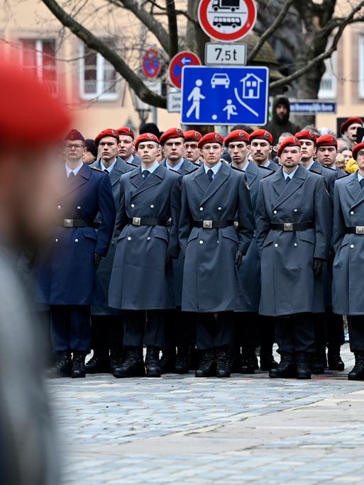 Ein öffentliches Gelöbnis der Bundeswehr mit Rekrutinnen und Rekruten, die rote Barrette tragen. 