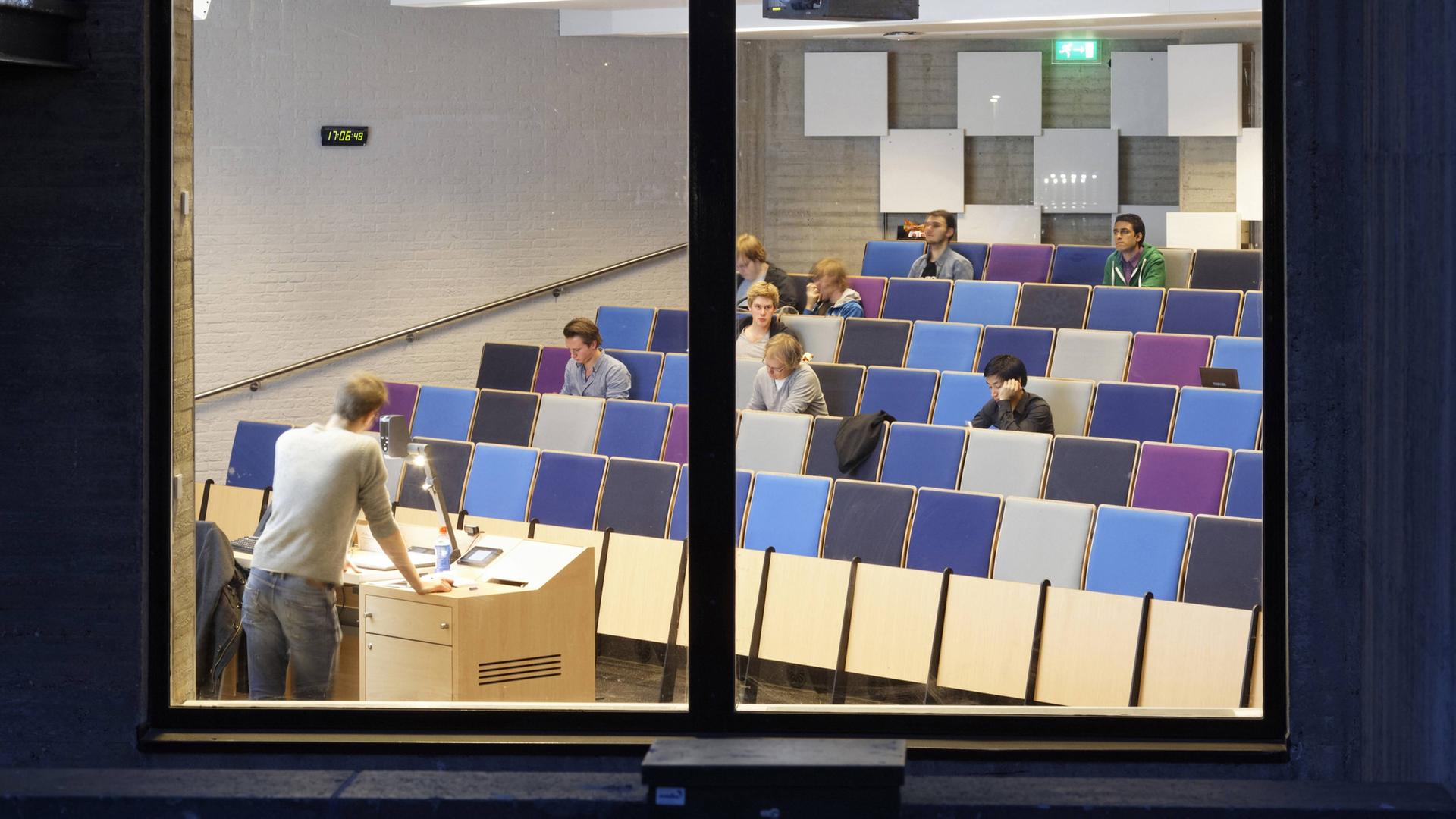 Blick durch ein Fenster in einen Hörsaal der Erasmus Universität in Rotterdam. Auf den Bänken sitzen einige Studierende. Vorne hält jemand einen Vortrag. Blick durch ein Fenster in einen Hörsaal der Erasmus Universität in Rotterdam. Auf den Bänken sitzen einige Studierende. Vorne hält jemand einen Vortrag.