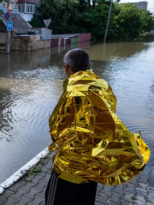 Bewohner von Cherson blicken auf die Überschwemmung in einer Straße. Sie sind in goldene Schutzfolien gehüllt, um sich zu wärmen. 
