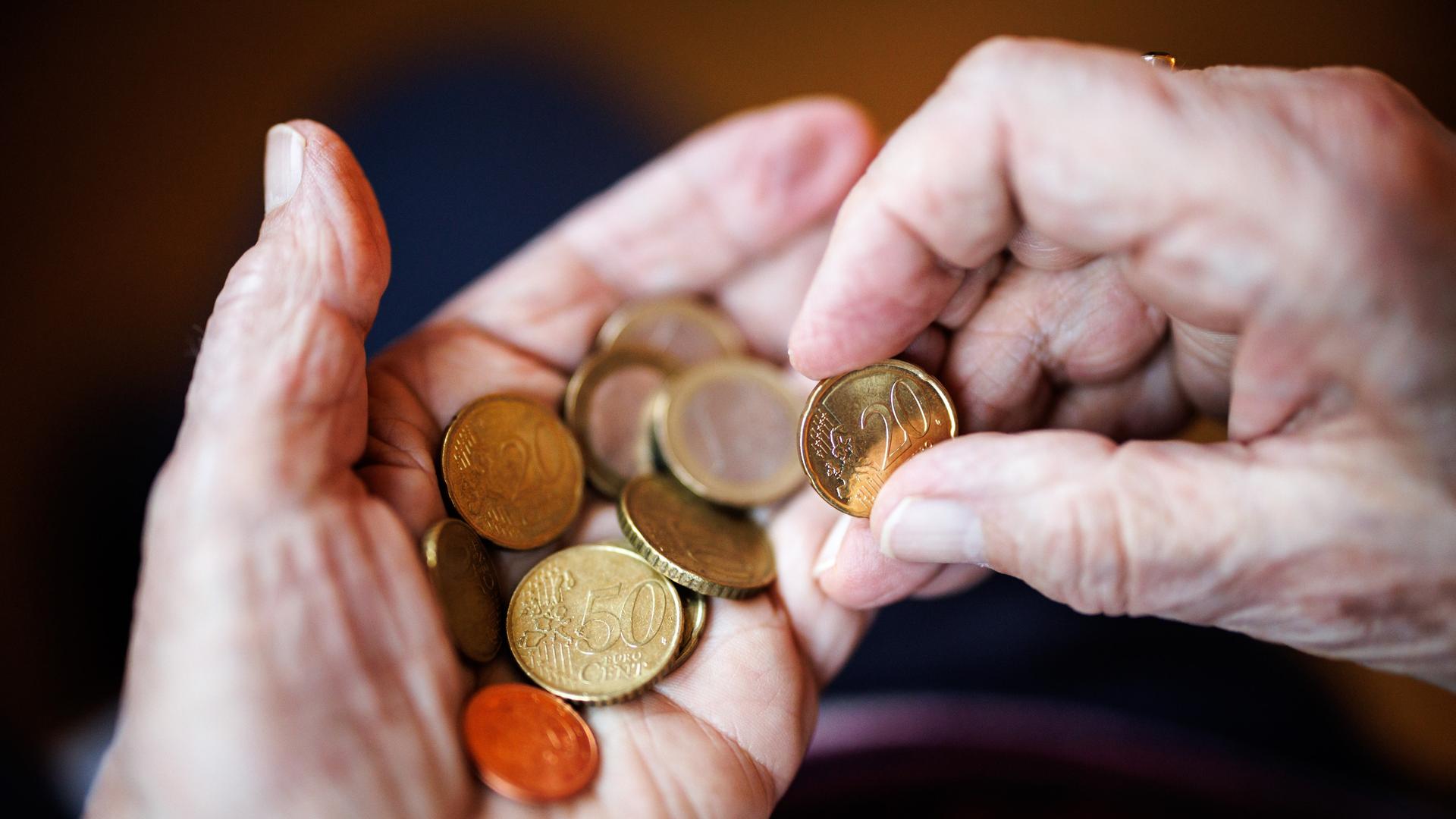 Eine ältere Dame zählt in ihren Händen das Bargeld aus ihrem Portemonnaie ab.