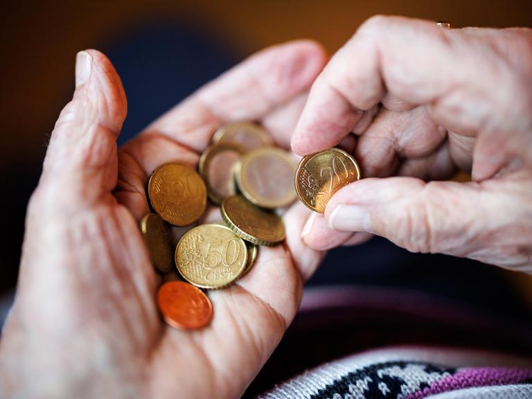 Eine ältere Dame zählt in ihren Händen das Bargeld aus ihrem Portemonnaie ab.