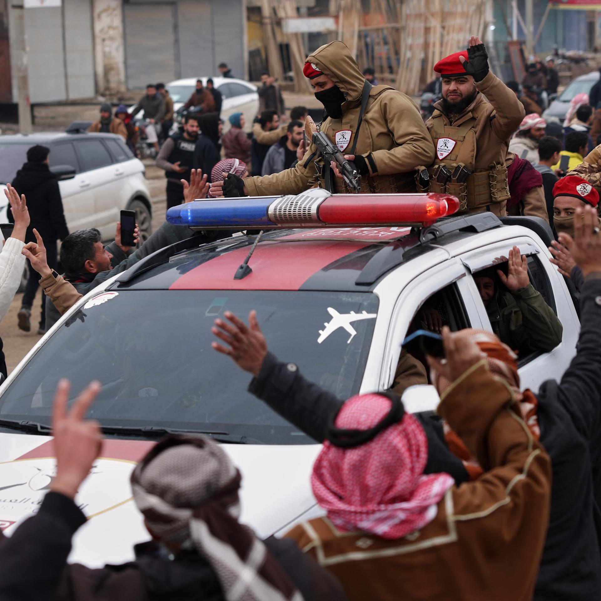 Truppen der syrischen Armee fahren mit Autos in eine Stadt, die sie eingenommen haben. Sie werden von den Einwohnern begrüßt.