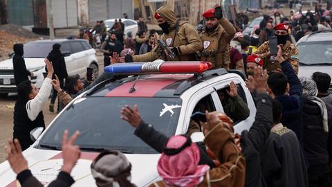 Truppen der syrischen Armee fahren mit Autos in eine Stadt, die sie eingenommen haben. Sie werden von den Einwohnern begrüßt.