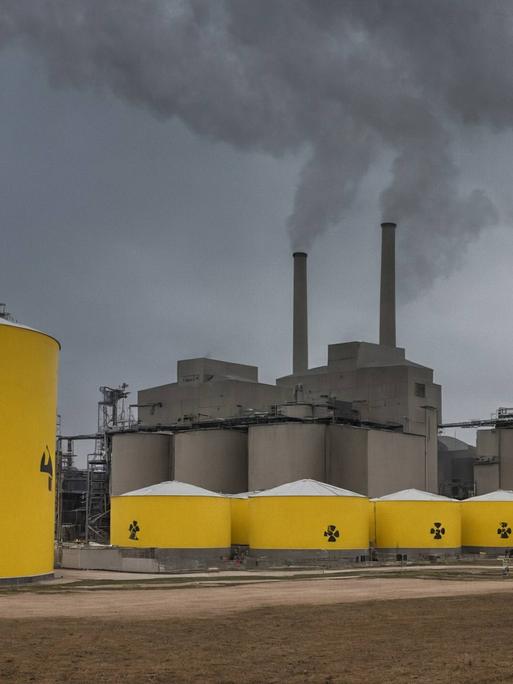 Atomkraftwerk mit Abfallfässern. Industriekraftwerk mit Kühltürmen und gelben Fässern mit radioaktivem Abfall auf einem Feld unter bewölktem Himmel.