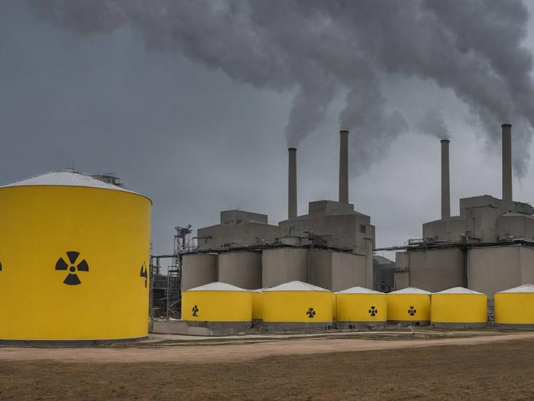 Atomkraftwerk mit Abfallfässern. Industriekraftwerk mit Kühltürmen und gelben Fässern mit radioaktivem Abfall auf einem Feld unter bewölktem Himmel.