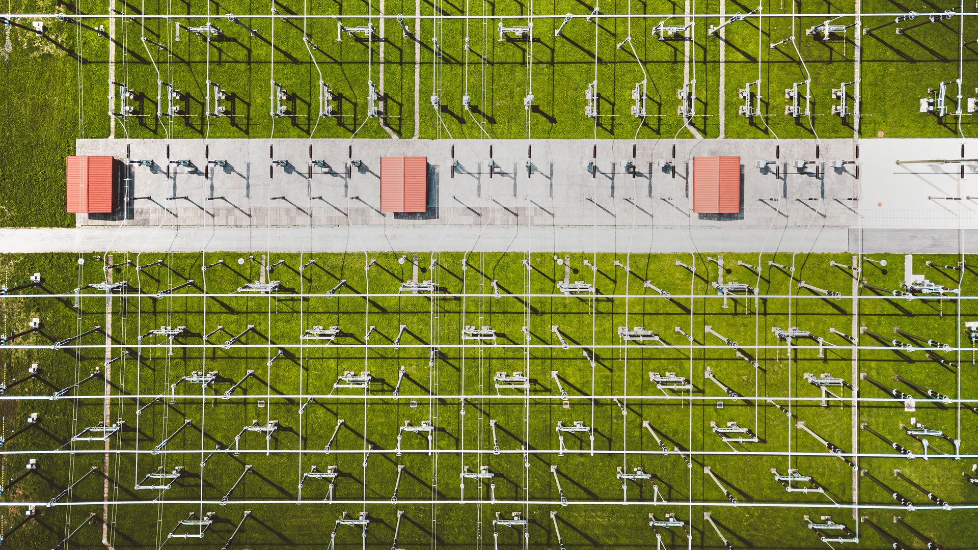 Luftbild auf ein Umspannwerk. Die Spannungsleitungen durchziehen die Wiese mit einem rasterartigen Muster.