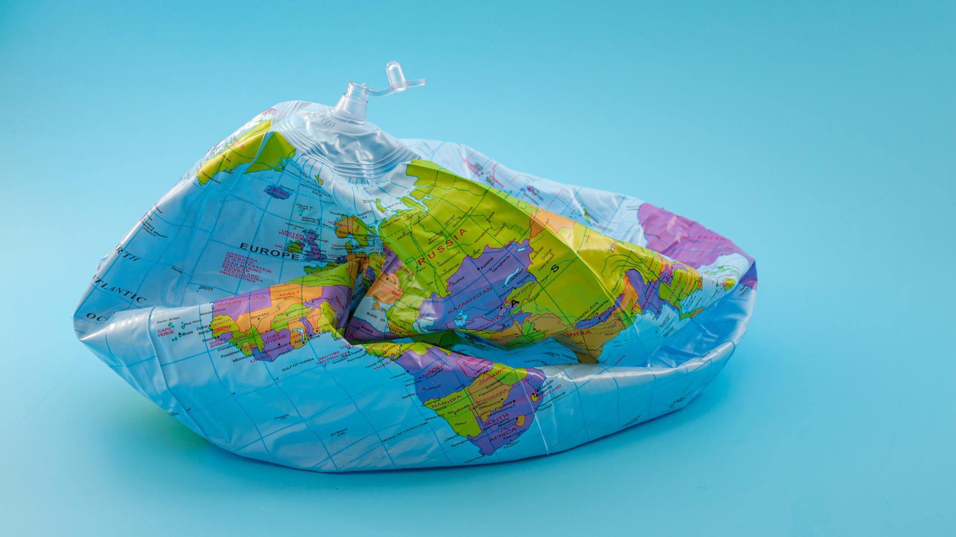 Ein zusammengefallener Ballon bedruckt mit dem Motiv eines Globus auf blauem Hintergrund. Ein zusammengefallener Ballon bedruckt mit dem Motiv eines Globus auf blauem Hintergrund.