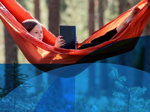 Ein junges Mädchen liegt in einer Hängematte und liest ein Buch.