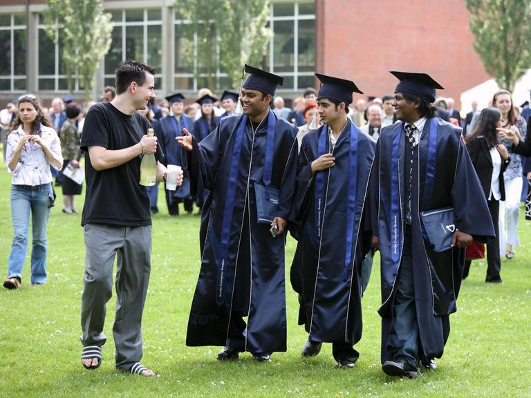 Abschlussfeier an der Uni in Bremen. Junge Menschen mit Doktorhüten gehen fröhlich über eine Wiese.