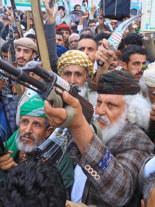 Sehr agitierte Anhänger der Huthi-Rebellen erheben ihre Waffen und führen drohende Gesten aus