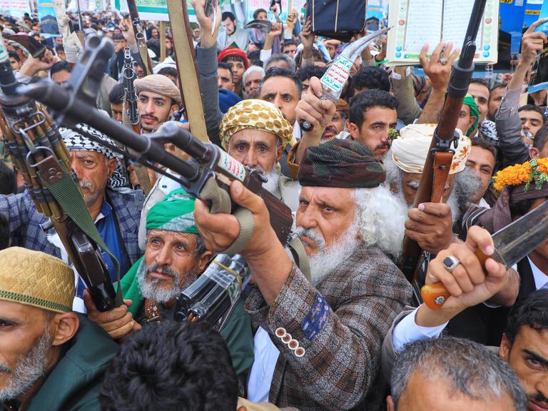 Sehr agitierte Anhänger der Huthi-Rebellen erheben ihre Waffen und führen drohende Gesten aus
