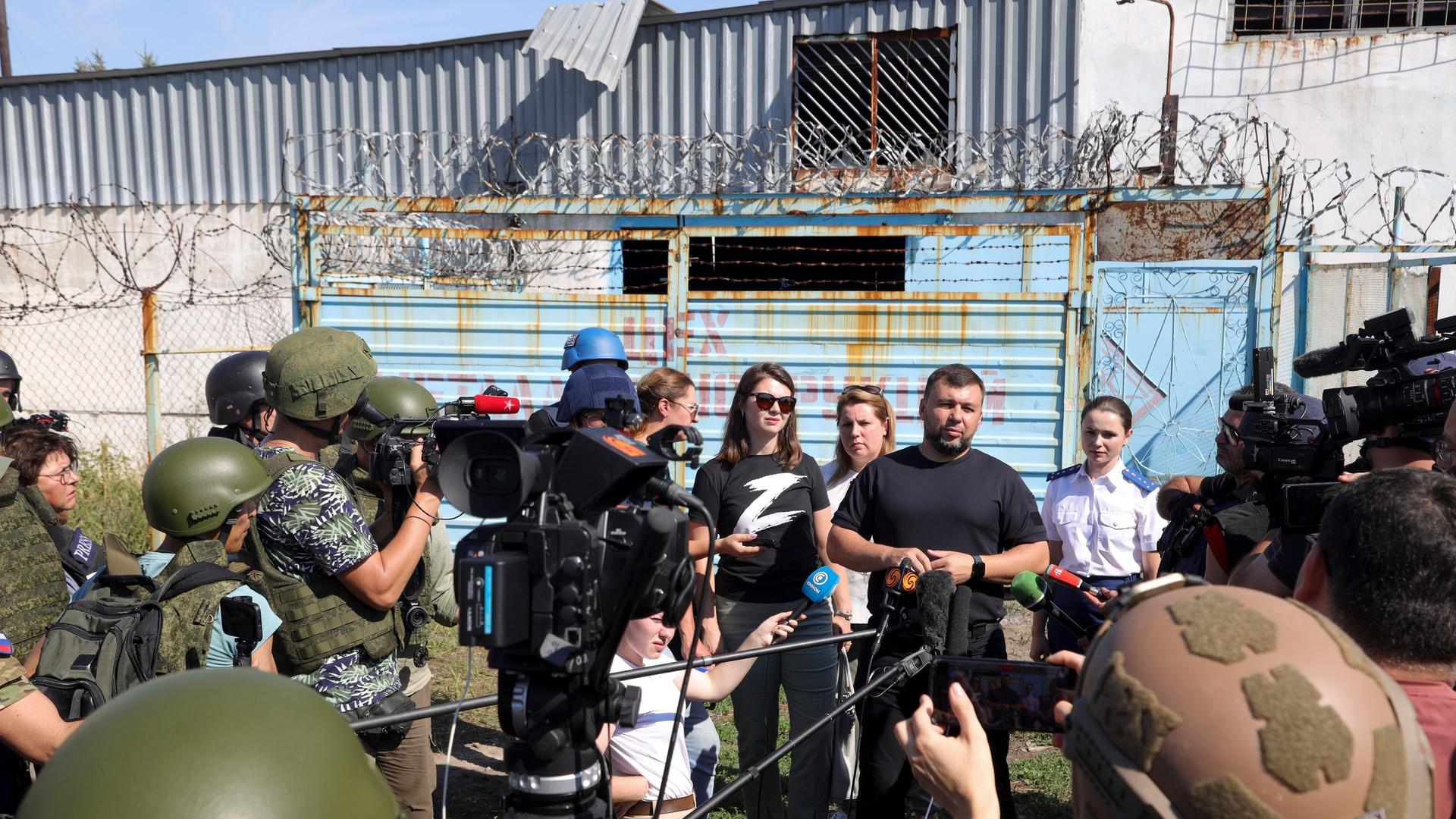 Denis Pushilin, the leader of the Donetsk People's Republic, background second right, speaks to foreign journalists at the destroyed barrack by following a strike on a prison housing POWs in Olenivka during a trip organized by the Russian Ministry of Defense, on the territory which is under the Government of the Donetsk People's Republic control, eastern Ukraine, Wednesday, Aug. 10, 2022. Russia has claimed that Ukraine's military used U.S.-supplied rocket launchers to strike the prison in Olenivka, a settlement controlled by the Moscow-backed Donetsk People's Republic. The Ukrainian military denied making any rocket or artillery strikes in Olenivka. (AP Photo)