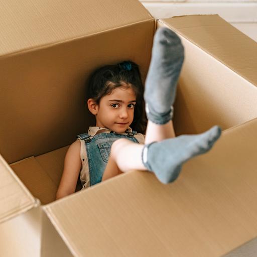 Kleines Mädchen liegt in einem Pappkarton und lächelt. 