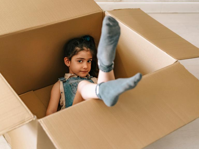 Kleines Mädchen liegt in einem Pappkarton und lächelt. 